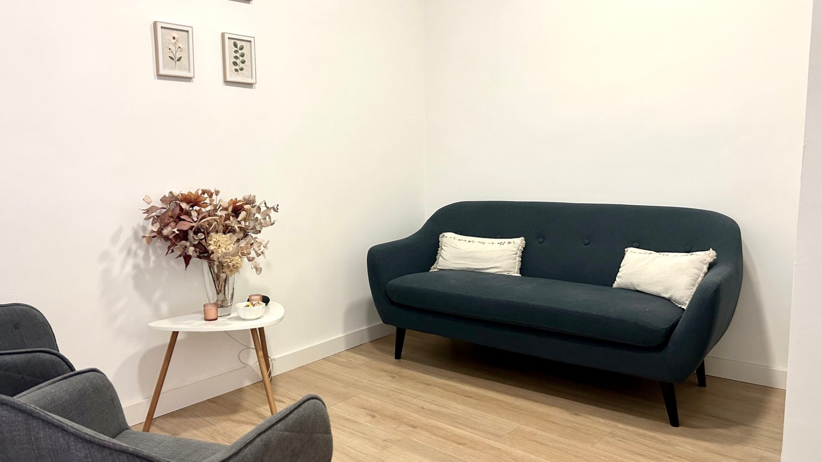 Una sala de la consulta: un sofá azul con cojines, dos butacas y una mesita con flores secas